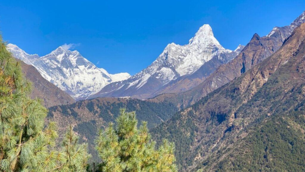 Snow-capped Himalayan peaks and lush green hills along the Everest Base Camp Trek route in Nepal under a clear blue sky.