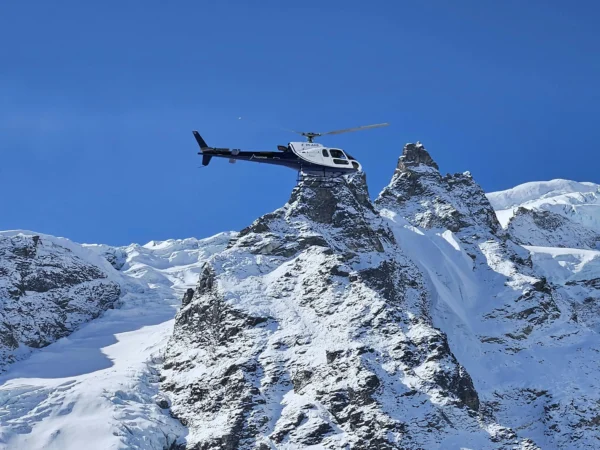 A helicopter soars above snow-covered Himalayan peaks against a clear blue sky in Koshi Province, Nepal