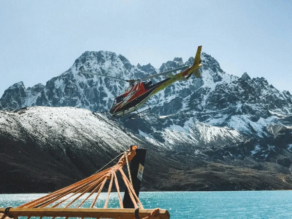 A vibrant helicopter flies over a tranquil lake framed by majestic Himalayan peaks in Nepal