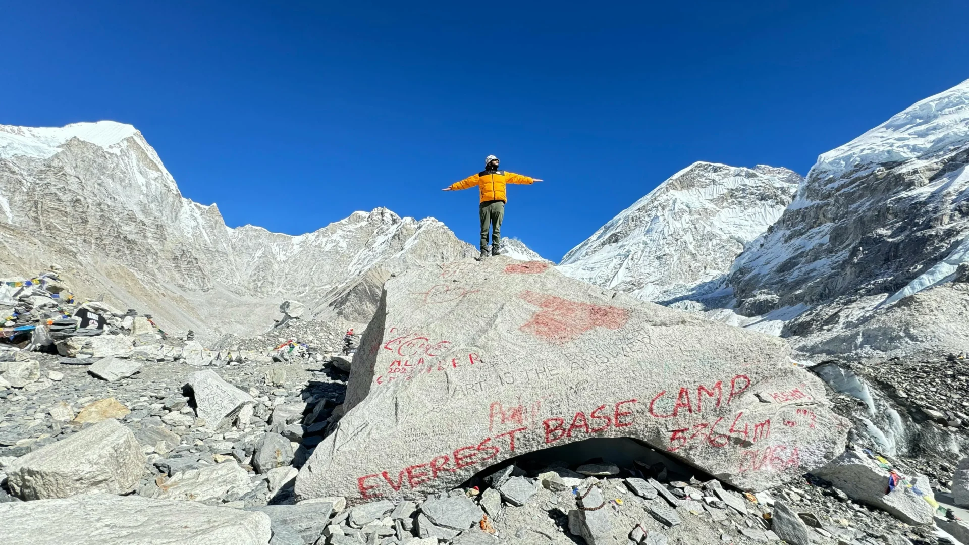 A mountaineer stands on a rock at Everest Base Camp, surrounded by snowy peaks