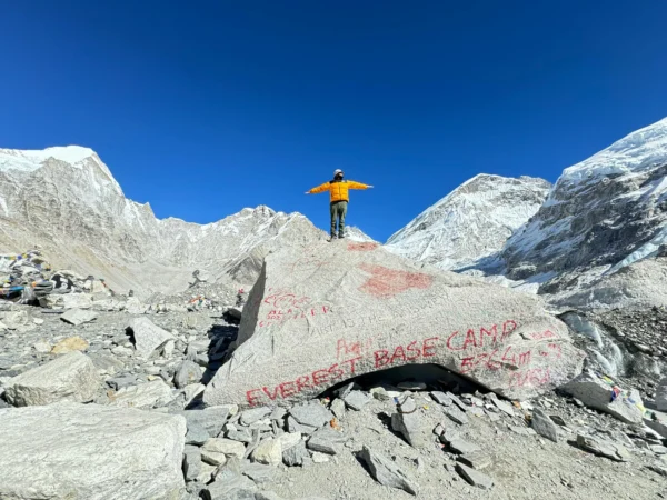A mountaineer stands on a rock at Everest Base Camp, surrounded by snowy peaks